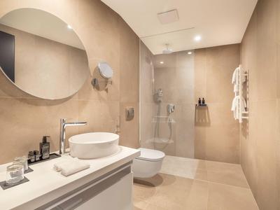 Modernes Badezimmer mit runder Glasdusche, weißem Waschbecken und großem ovalem Spiegel.