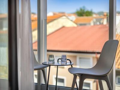 Moderner Stuhl und runder Tisch vor einem Fenster mit Blick auf Dächer und blauen Himmel.