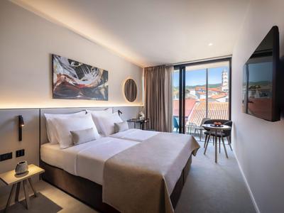 Hell eingerichtetes Hotelzimmer mit zwei Betten, großem Fenster und Blick auf die Stadt.