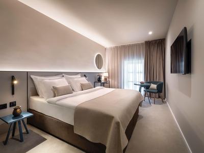 Modern eingerichtetes Hotelzimmer mit großem Bett, Schreibtisch und TV an der Wand.