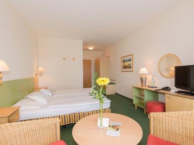 Hotelkamer met tweepersoonsbed, tv, tafel met stoelen en bloemenvaas.