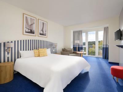 Nowoczesny pokój hotelowy z białym łóżkiem, balkonem i niebieskim dywanem.