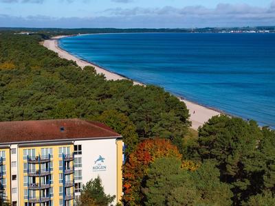Budynek hotelu na skraju lasu z widokiem na długą piaszczystą plażę i niebieskie morze.