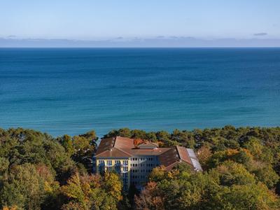 Budynek hotelu otoczony gęstą zielenią z szerokim widokiem na niebieskie morze.