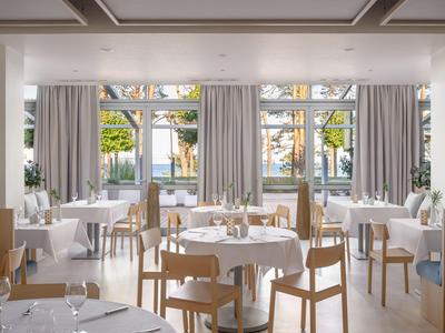 Jasna, nowoczesna restauracja hotelowa z białymi obrusami, drewnianymi krzesłami i dużymi oknami z widokiem na ogród.
