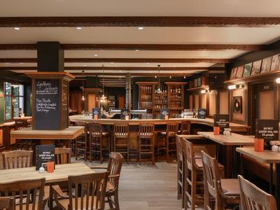 Rustykalny bar hotelowy z drewnianymi meblami, oświetlonym barem i przytulną atmosferą.