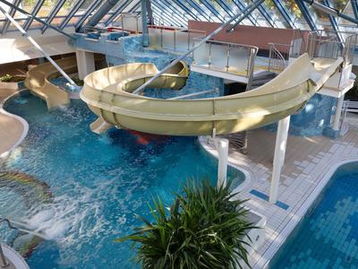 Wnętrze hotelu z zjeżdżalnią i basenami pod szklanym dachem.