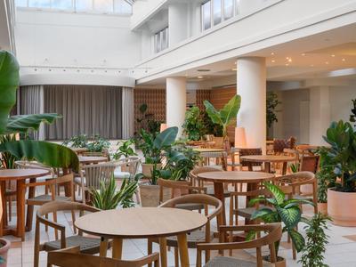 Jasna, nowoczesna jadalnia hotelowa z drewnianymi krzesłami, stołami i licznymi zielonymi roślinami.