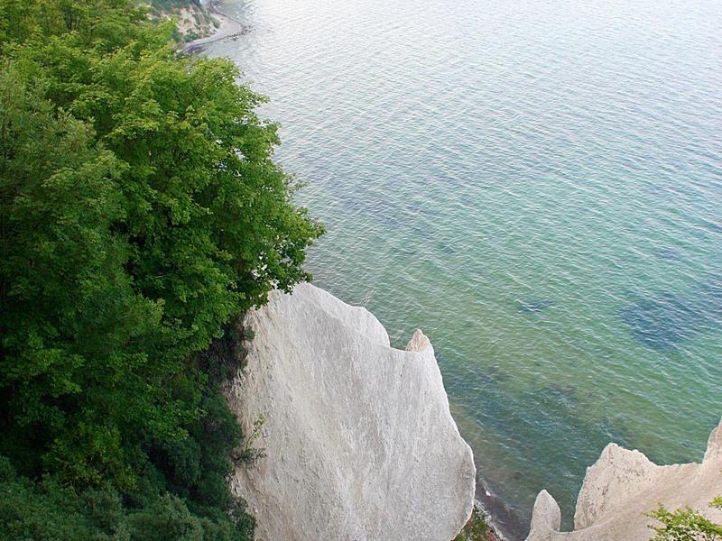 Steile weiße Kreidefelsen mit grünem Bewuchs neben klarem, ruhigem Meer unter hellem Himmel.