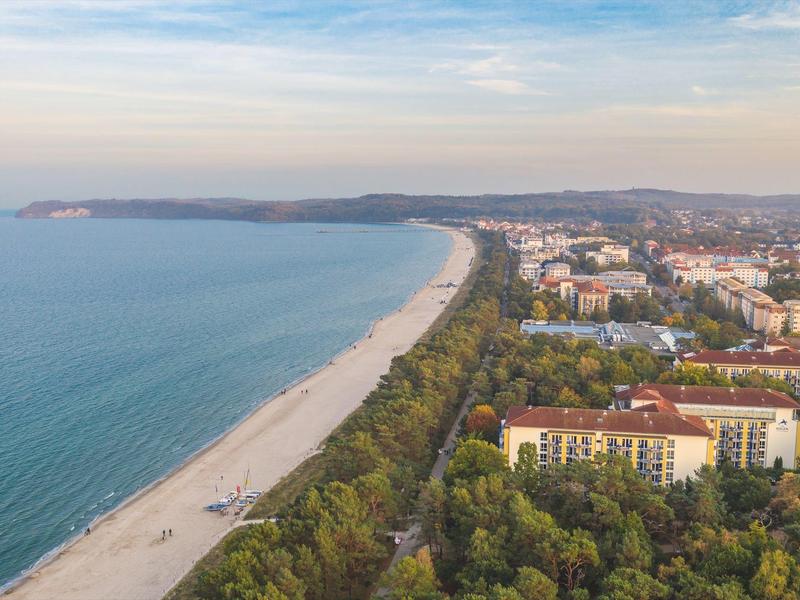 Langer Sandstrand neben grünen Bäumen und Gebäuden unter blauem Himmel am Meer.