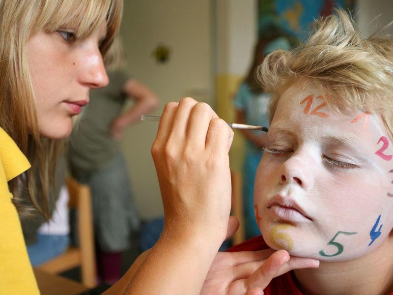 Ein Mädchen malt mit Pinsel Zahlen auf das Gesicht eines Jungen, der die Augen geschlossen hat.