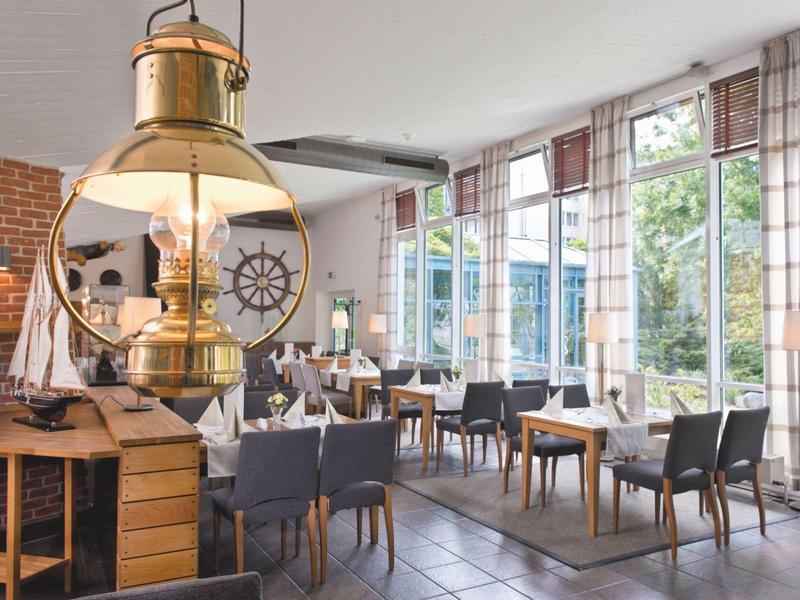 Helles Restaurant mit großen Fenstern, Holztischen, grauen Stühlen und maritimer Dekoration.