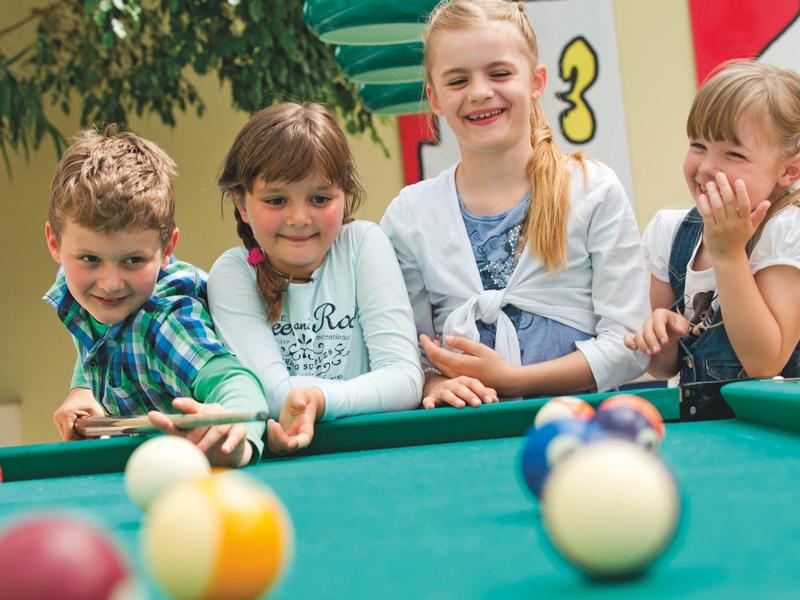 Vier Kinder spielen fröhlich an einem grünen Billardtisch mit bunten Kugeln.