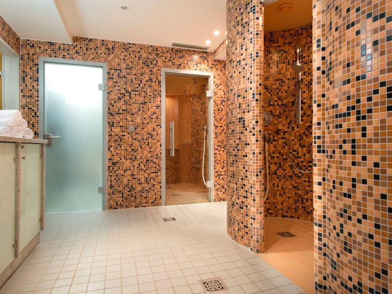 Großer Duschraum mit orange-schwarzen Mosaikfliesen, weißen Bodenfliesen und zwei Duschen.