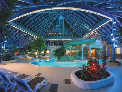 Moderner Innenpool in einem Hotel mit gläsernem Dach und tropischer Beleuchtung.