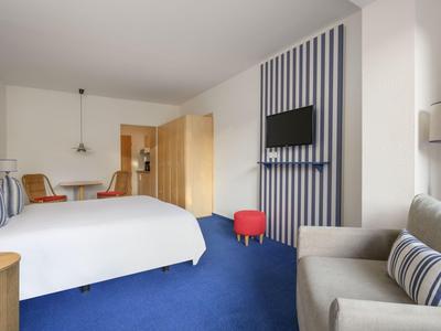 Modern hotel room with blue carpet, double bed, and seating area.
