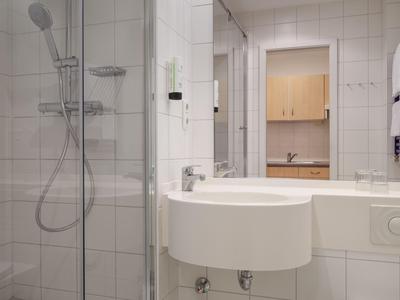 Modern hotel bathroom with round sink, shower, and light-colored tiles.