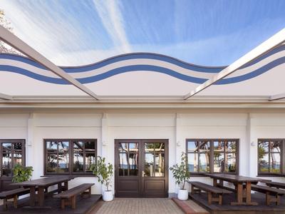 Modern hotel outdoor area with wooden benches and decorative plants under wavy roofs.