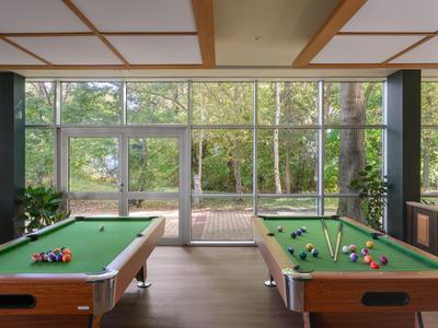Room with two pool tables and large windows overlooking a terrace and trees.