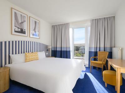 Modern hotel room with large bed, blue and white striped wall, and balcony with view.