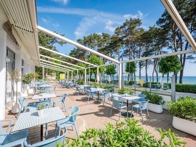 Terrace with blue chairs and tables beside a hotel, overlooking trees and the sea.