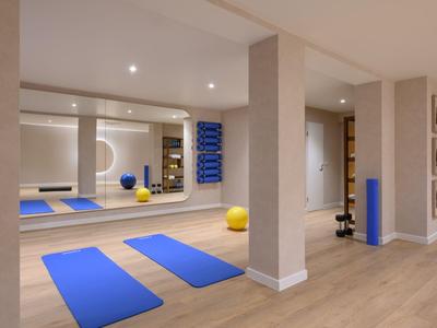 Modern fitness room with blue yoga mats and mirrored wall in a hotel.
