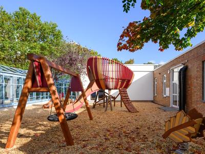 A modern playground with wooden swing and slide in a sunny hotel courtyard.