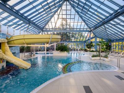 Indoor pool with water slide, palm trees, and large glass windows in a hotel