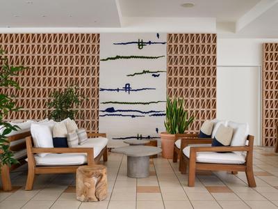 Bright hotel lounge with wooden armchairs, white cushions, and modern wall decorations.
