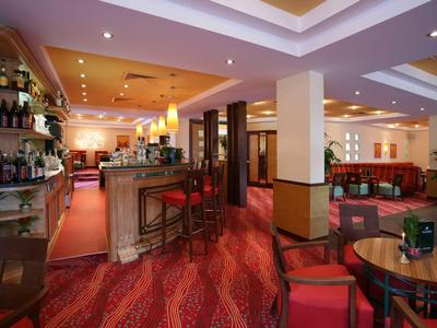 Innenansicht einer Hotelbar mit roten Teppichen, Tischen, Stühlen und beleuchteter Theke.