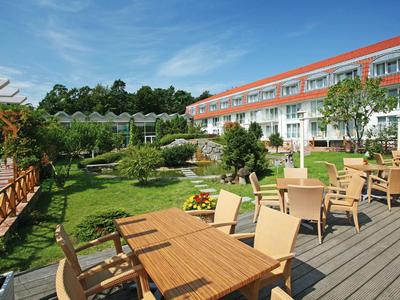 Terrassenbereich eines Hotels mit Holzmöbeln und Blick auf gepflegte Gartenanlagen.