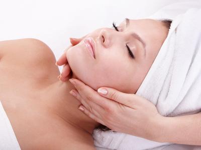Frau entspannt bei einer Gesichtsmassage im Wellnesshotel mit Hand und Handtuch am Kopf.