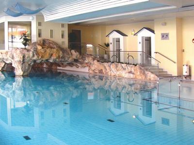 Innenpool in einem hellen Raum mit einem künstlichen Wasserfall und einem Sitzbereich.