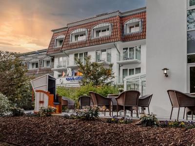 Venkovní posezení hotelu se židlemi a stoly obklopené stromy a vícepodlažní budovou.