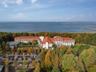 Hotelový komplex s červenými střechami uprostřed podzimně zbarveného lesa na pobřeží.
