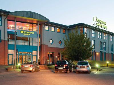 Modernes, mehrstöckiges Hotelgebäude mit beleuchtetem Eingang und geparkten Autos davor bei Dämmerung.