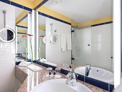 Modernes Badezimmer mit Waschbecken, großer Spiegelwand, Badewanne und weißen Wandfliesen.