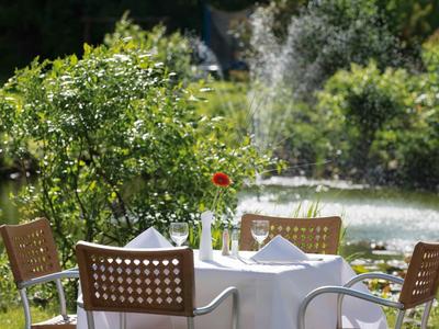Runder Tisch mit weißer Tischdecke, vier Stühlen und Blumen im Garten bei Sonnenschein.