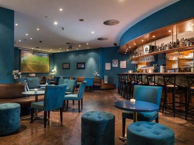 Gemütliche Bar mit blauen Wänden, Sitzgruppen, Hockern und Holzfußboden, warm beleuchtet.