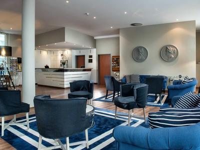 Moderne Lounge mit blauen Sesseln, einem Teppich und stilvollen Lampen in hellem Raum.