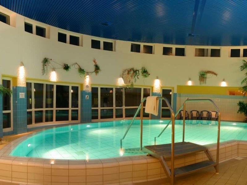 Innenpool mit türkisfarbenem Wasser, Liegestühlen, Palmen und hellem Deck in rundem Raum.