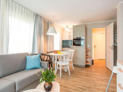 Modern eingerichtetes Wohnzimmer mit Sofa, Esstisch und offener Küche in warmen Farbtönen.