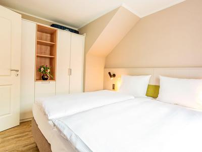 Helles Hotelzimmer mit großem Doppelbett, weißen Wänden und modernem Holzschrank.