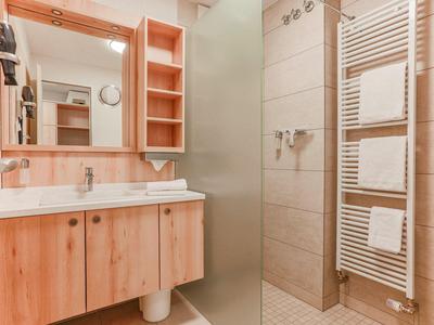 Modernes Badezimmer mit Holzschrank, großem Spiegel und beiger Fliesendusche.