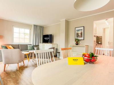 Helles Hotelzimmer mit Essbereich, Sitzecke, Fernseher und Blick auf Küche.