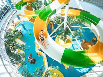 Blick auf eine bunte Wasserrutsche in einem Hotel oder Ferienresort mit Personen, Pflanzen und Poolbereich.