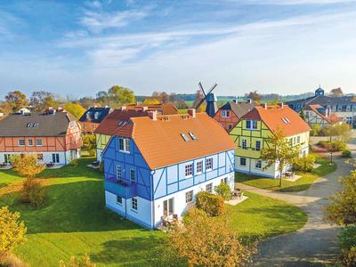 Dorf mit Fachwerkhäusern und grünen Gärten unter blauem Himmel an einem sonnigen Tag.