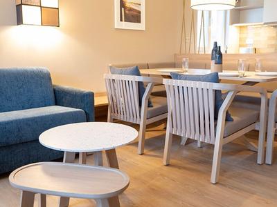 Bright living area with blue sofa, round tables, dining table, and chairs in a hotel room.