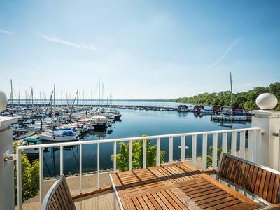 View from a balcony with wooden table overlooking a harbor with boats under clear sky.