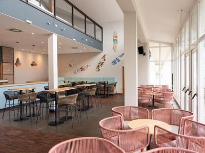 Modern hotel area with pink chairs, wooden tables, and large glass windows.